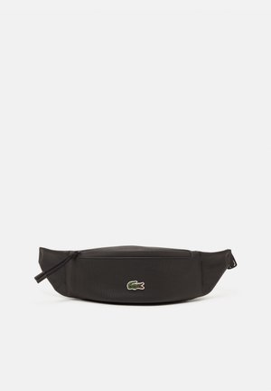 Sac banane en tissu noir avec fermeture éclair à l'avant et petit logo crocodile vert au centre sur fond blanc.