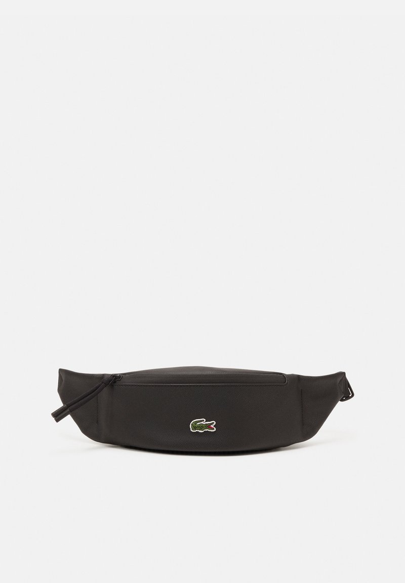 Sac banane en tissu noir avec fermeture éclair à l'avant et petit logo crocodile vert au centre sur fond blanc.
