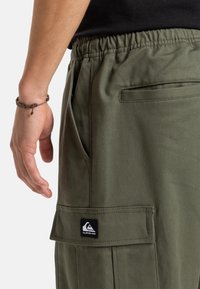 Khaki zelené cargo šortky s texturovanou tkaninou, elastickým pasem, bočními kapsami a nášivkou na levé nohavici.