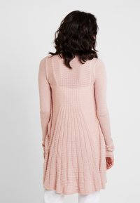 Långärmad cardigan i mjuk rosa stickning, med en strukturerad ribbad design och veckad bakdel för ökad volym och flöde.