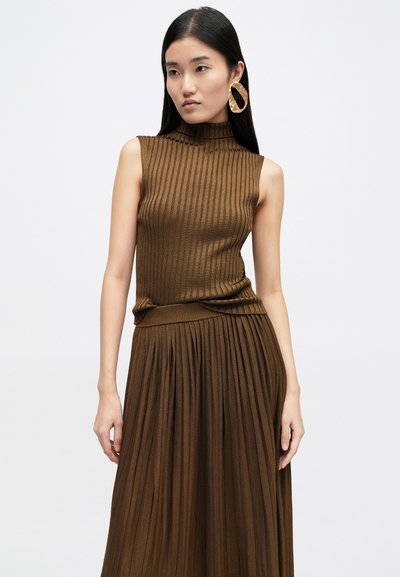 Brown ribbed sleeveless top paired with a pleated brown skirt, featuring a high neck design and textured fabric. Large gold hoop earrings.