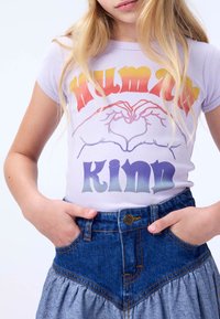 Lilla kortermet T-skjorte med hjerteformet håndgrafikk, med "KVINNER" i oransje og "KINN" i gradient lilla bokstaver. Kombinert med et jeansskjørt.