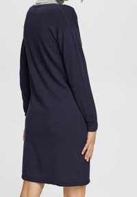 Marinblå stickad klänning med långa ärmar, rund krage och ribbad nederkant. Figursydd form och mjuk textur, med en enkel och ren design.