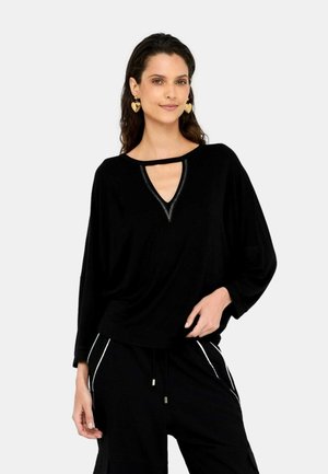 Top nero a maniche lunghe con scollo a V e dettagli ritagliati, caratterizzato da una vestibilità comoda e una leggera lucentezza. Abbinato a pantaloni neri con accenti bianchi.