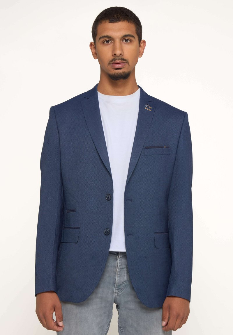 Blazer bleu marine en tissu texturé, à deux boutons et avec une poche poitrine unique. Il comprend deux poches latérales et un accent de broche au revers.