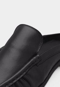 Mocassin noir en cuir à enfiler avec coutures moc toe et finition lisse, présenté en gros plan sur un fond clair uni.