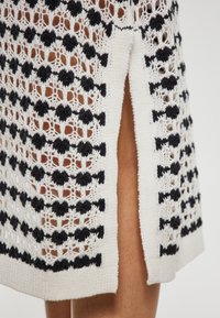Rochie tricotată cu un model asemănător dantelei în alb și negru, cu țesătură texturată și o fante laterală pentru un design detaliat.