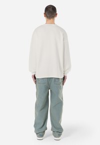 Hvid, struktureret oversized langærmet skjorte parret med lyseblå, rummelige denimbukser. Bagfra ses det afslappede fit og sænkede skuldre.