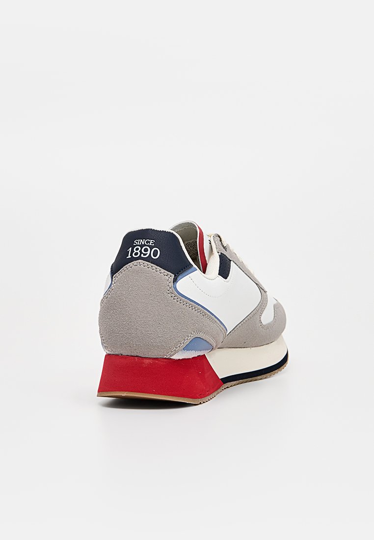 Zapatilla de ante gris con acentos en blanco, azul marino y rojo. Presenta un tacón redondeado y material texturizado, con detalles de diseño cerca del tobillo.