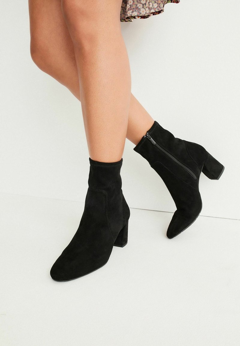 Bottes noires en daim à cheville avec un bout pointu, une fermeture éclair sur le côté et un talon bloc, offrant un ajustement serré à la cheville.