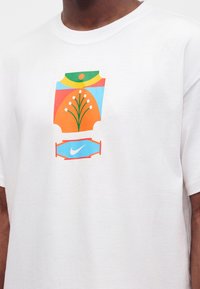 Άνδρας που φοράει λευκό T-shirt με πολύχρωμο αφηρημένο σχέδιο και μικρό λογότυπο Nike Swoosh στο κέντρο της θωρακικής περιοχής.