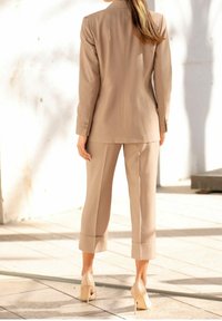 Beige dobře padnoucí oblek s dlouhým sáčkem a krátkými kalhotami. Hladká textura, zapínání na jeden knoflík, doplněno nahými lodičkami na vysokém podpatku.