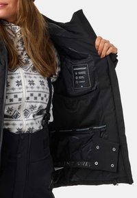 Giacca impermeabile nera con rivestimento interno a fantasia. Presenta un'etichetta di cura, tasca in rete e dettagli in Velcro sui polsini.