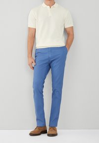 Beige kortärmad pikétröja med krage, tillsammans med ljusblå slim-fit byxor och bruna mockaskor.