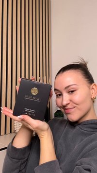 Musta laatikko, jossa on kultaista logoa ja teksti "Velvet Oud", sisältäen tuoksukynttilän. Taustalla puiset luisut. Kädet pitävät tuotetta rentossa asennossa.