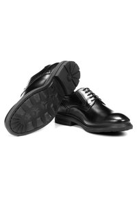 Chaussures de ville en cuir noir avec une finition lisse, un design à bout d'aile et une semelle en caoutchouc crantée. Lacets avec œillets pour un maintien sécurisé.