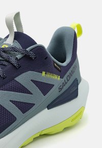 Lilla og grå sneaker med mesh og semsket skinn, med limegrønne detaljer, teksturerte lisser og en hvit mellomsåle med gripe såle.