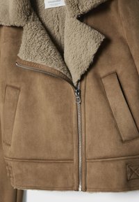 Brązowa zamszowa kurtka z beżowym kołnierzem z sztucznego baranka, zamkiem błyskawicznym oraz dwoma bocznymi kieszeniami. Posiada krótki krój i ozdobne przeszycia.