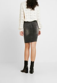 Jupe en denim gris à coupe ajustée, avec deux poches arrière et une longueur mi-mollet, associée à un pull en laine crème et des bottes à talons noires.