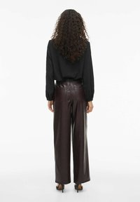 Haut texturé noir à manches longues associé à un pantalon large en cuir bordeaux et des chaussures à talons hauts noires, vu de derrière.