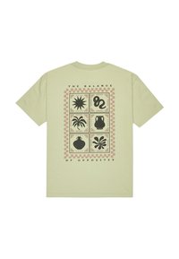 Světle zelené bavlněné tričko s černým grafickým potiskem různých tvarů uspořádaných do mřížky, s textem "ROVNOVÁHA OPOZITŮ" nahoře.