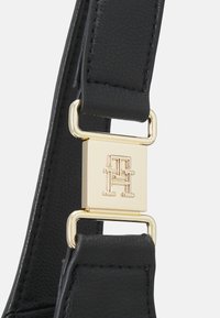 Czarny skórzany pasek o fakturze z złotym prostokątnym zapięciem z wytłaczanym przeplatającym się logo "TH".