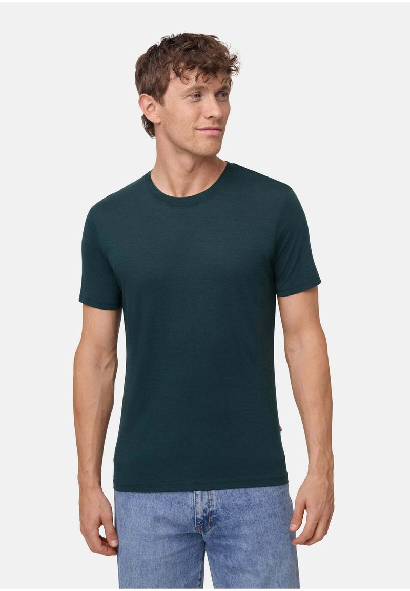 Dunkelgrünes T-Shirt mit Rundhalsausschnitt aus weichem Stoff, mit kurzen Ärmeln und einer figurnahen Silhouette. Kombiniert mit hellblauen Jeans.