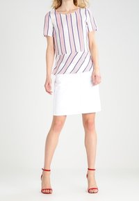 Gestreepte korte mouwen top in crème, marineblauw en koraal met een losse fit, gecombineerd met een witte rok tot de knie en rode hoge sandalen.