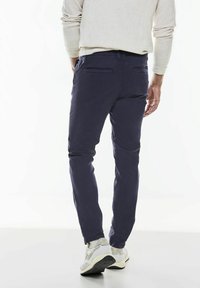 Chinos azul marino con un corte slim, que presentan una textura de algodón suave, dos bolsillos traseros y detalles de costura sutiles, combinados con zapatillas ligeras.