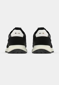 Μαύρα αθλητικά παπούτσια με υφασμένο επάνω μέρος, λευκές λεπτομέρειες στη φτέρνα και ανοιχτόχρωμη σόλα. Διαθέτουν μαξιλαρωμένο γιακά και γλώσσα.