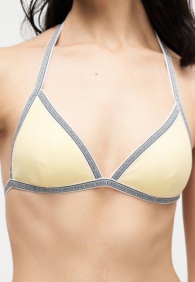 Femme portant un haut de bikini triangle jaune pâle avec une bordure à motifs noir et blanc et des bretelles nouées autour du cou.