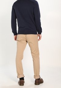 Pull marin à col rond, chinos beiges, revers roulés, chaussures marron. Texture douce, coupe ajustée, palette de couleurs neutres.