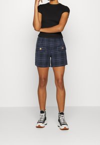 Black short-sleeve top paired with navy plaid shorts featuring two front pockets and gold buttons, complemented by high-top sneakers.