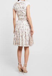 Bloemenpatroon jurk in lichte kleuren met kantafwerking, plissé rok en een stoffen riem. Gedragen met nude hoge hakken.