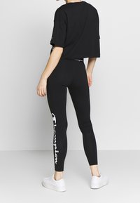 Czarny krótki t-shirt z krótkimi rękawami, zestawiony z czarnymi legginsami z wysokim stanem, z białym nadrukiem logo „Champion” biegnącym wzdłuż lewej nogawki. Białe sneakersy.