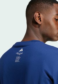 T-shirt a maniche corte blu navy con scollo a girocollo, caratterizzato da una grafica testuale bianca sul retro e tre strisce bianche vicino al collo.