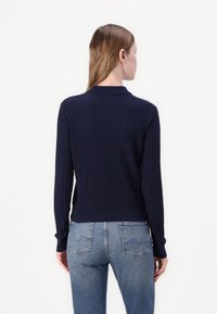 Sweater azul-marinho com nervuras, de mangas longas e colarinho, design ajustado. Usado com jeans azul-claro, mostrando a vista traseira e o tecido texturizado.