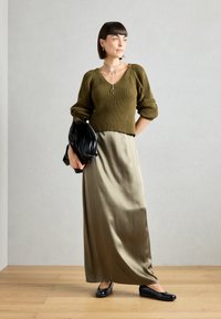 Pull en olive côtelé, jupe maxi satinée olive, sac à main noir et ballerines noires. Design minimal, coupe décontractée, texture lisse.