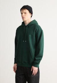 Sudadera verde hecha de una mezcla de algodón, con un bolsillo canguro, capucha con cordón ajustable y logo bordado en el pecho.