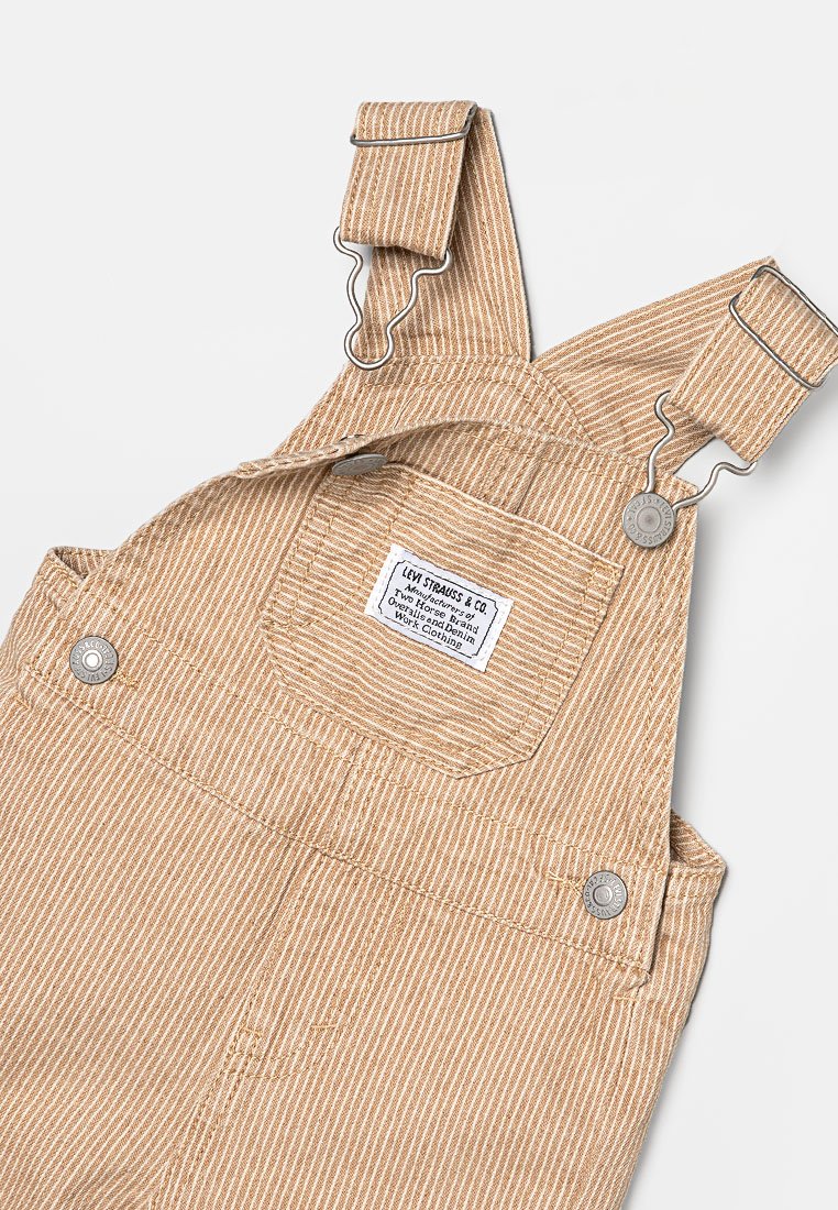 Beige gestreifte Latzhose aus strukturiertem Stoff mit verstellbaren Metallclips, einer Brusttasche und einem Markenetikett auf der Brust.