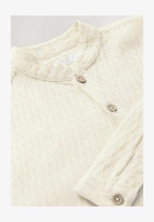 Šviesios spalvos, tekstūruota marškinė su mandarinų apykakle, turinti du medinius mygtukus ir subtilesnį lapų raštą.