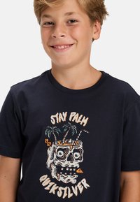 Granatowa bawełniana koszulka z kolorowym nadrukiem czaszki z palmami i drinkiem. Okrągły dekolt i krótkie rękawy.