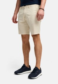 Beige katoenen shorts met rechte snit, voorzakken en een knoopsluiting, gecombineerd met donkerblauwe sneakers met witte zolen.
