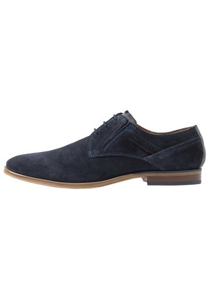 Męskie granatowe zamszowe eleganckie buty sznurowane z jasnobrązową podeszwą i niskim, nałożonym obcasem, bocznymi przeszyciami i wytłoczonym logo.