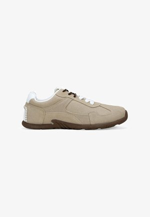 Beige suede sneaker with white accents, featuring brown laces, textured side panels, and a flexible brown rubber sole.