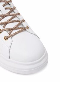 Sneaker bianca con tomaia in pelle liscia, dotata di occhielli metallici dorati e lacci dorati glitterati, punta rotonda e suola spessa bianca.