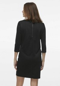 Svart klänning med trekvartsärmar och figurnära silhuett, med en dragkedja bak och slät tygkvalitet.