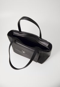 Borsa tote in pelle nera con manici lunghi, scomparto principale con zip, tasca esterna e discreto dettaglio del logo sul davanti. Texture liscia.