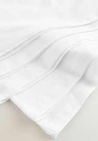Witte katoenstof, gevouwen met zichtbare textuur en stiksels, met een gladde oppervlakte en een zachte uitstraling.