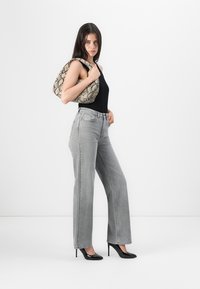 Grijze high-waisted wijde jeans, gestyled met een zwarte tanktop en een handtas met slangenpatroon, aangevuld met zwarte stilettos.
